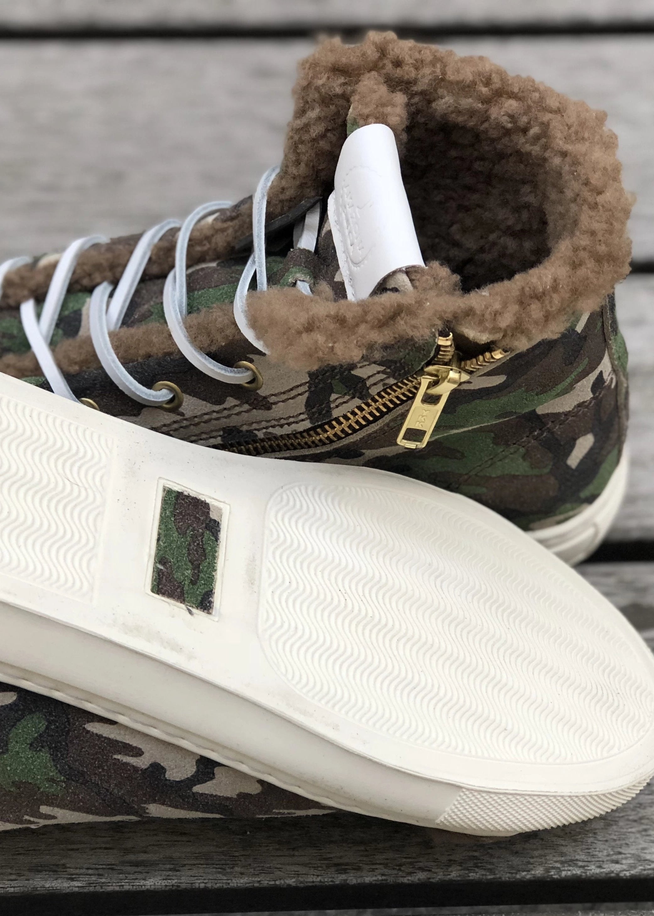 Camouflage high-top sneakers with white soles on a wooden surface